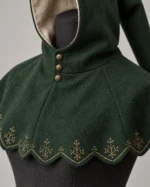 Forest green Aldric hood showing three brass throat buttons, golden botanical embroidery and the scalloped mantle edge