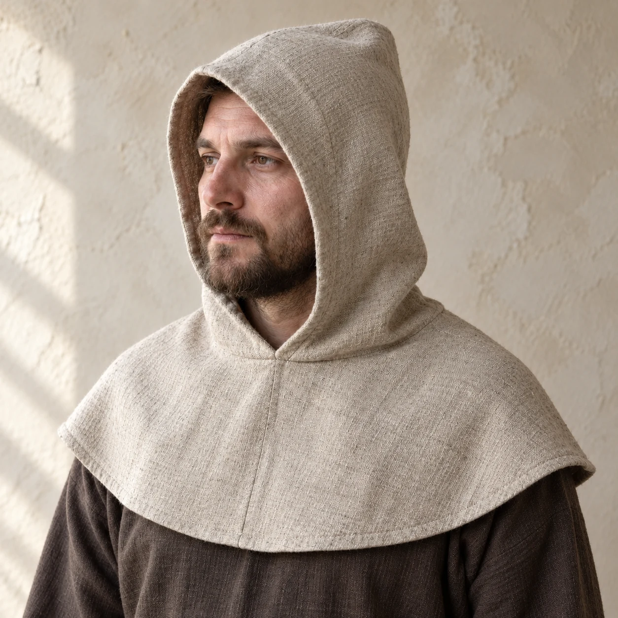 Oatmeal linen peasant hood with a rounded shoulder mantle, worn over a brown tunic